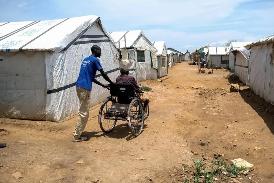 Man helping another using a wheelchair in a refugee camp