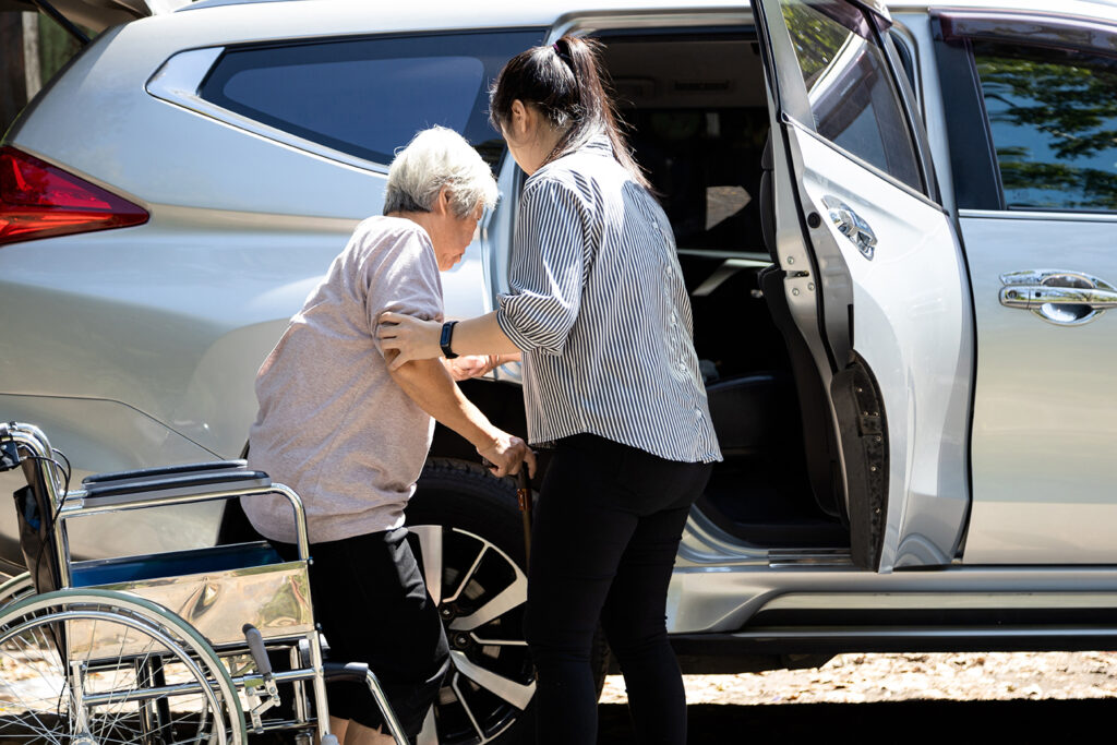 A daughter is helping her mother in wheelchair to get into the car.