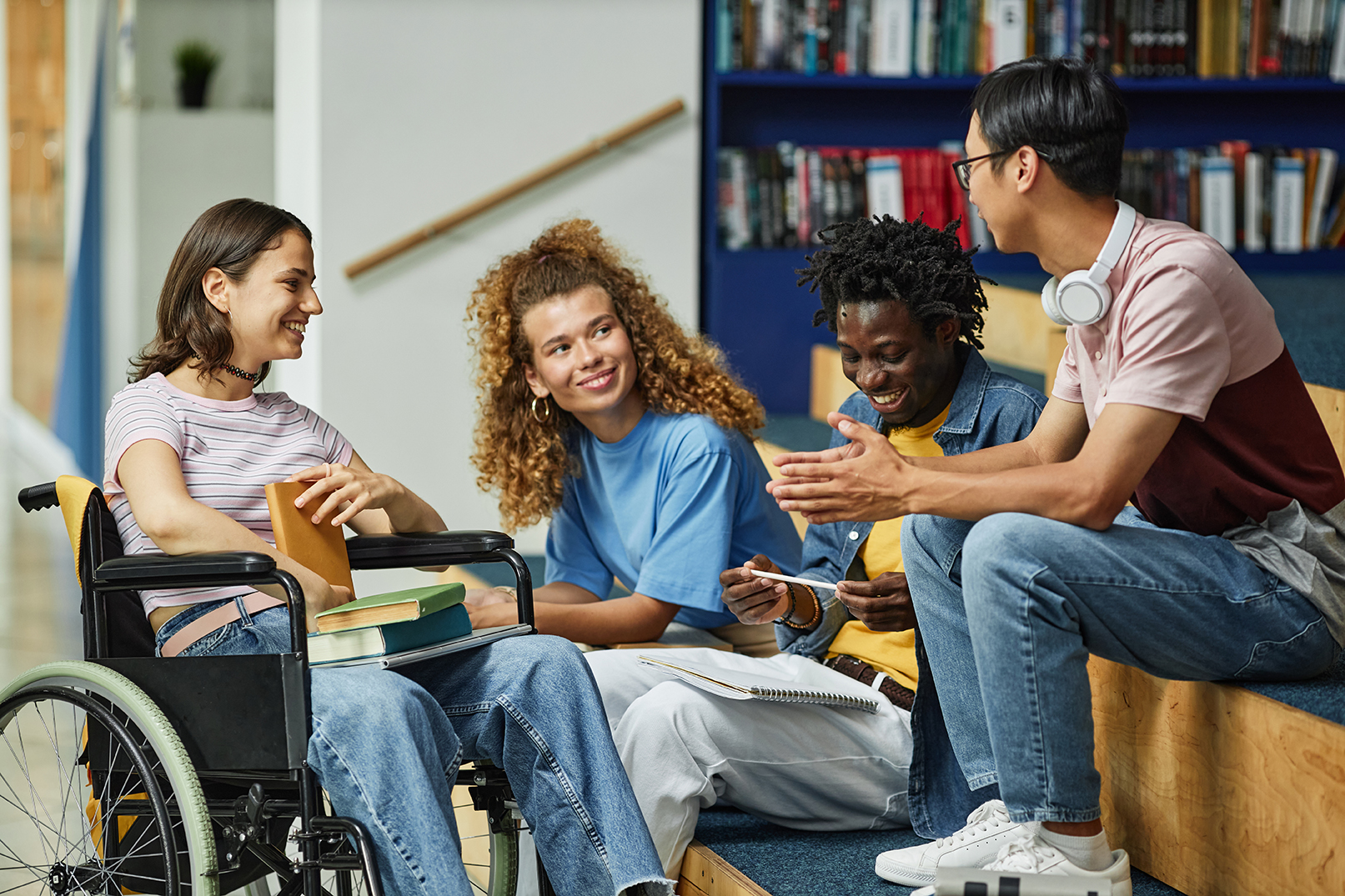 Diverse group of young people chatting in college library including female student with disability