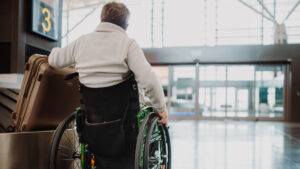 Rear view of a man on wheelchair at airport with his luggage.