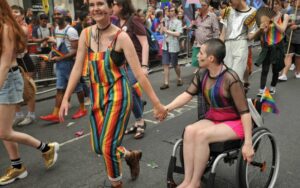 A Pride person walking with a Pride person using a wheelchair