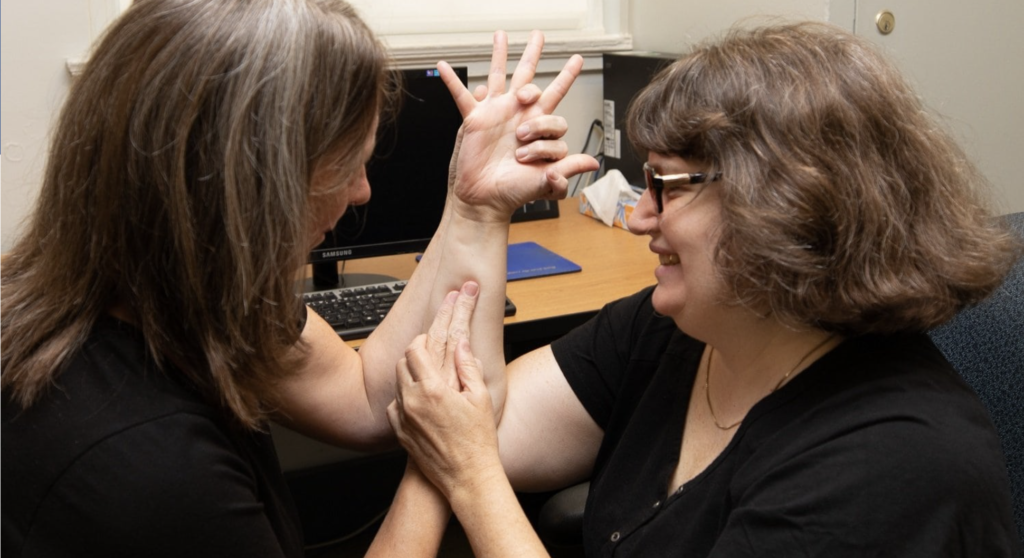 A Support Service Provider works with her client using tactile sign language. 