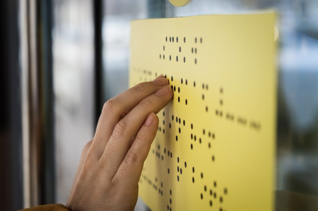 A person uses their fingers to read a sign in Braille.