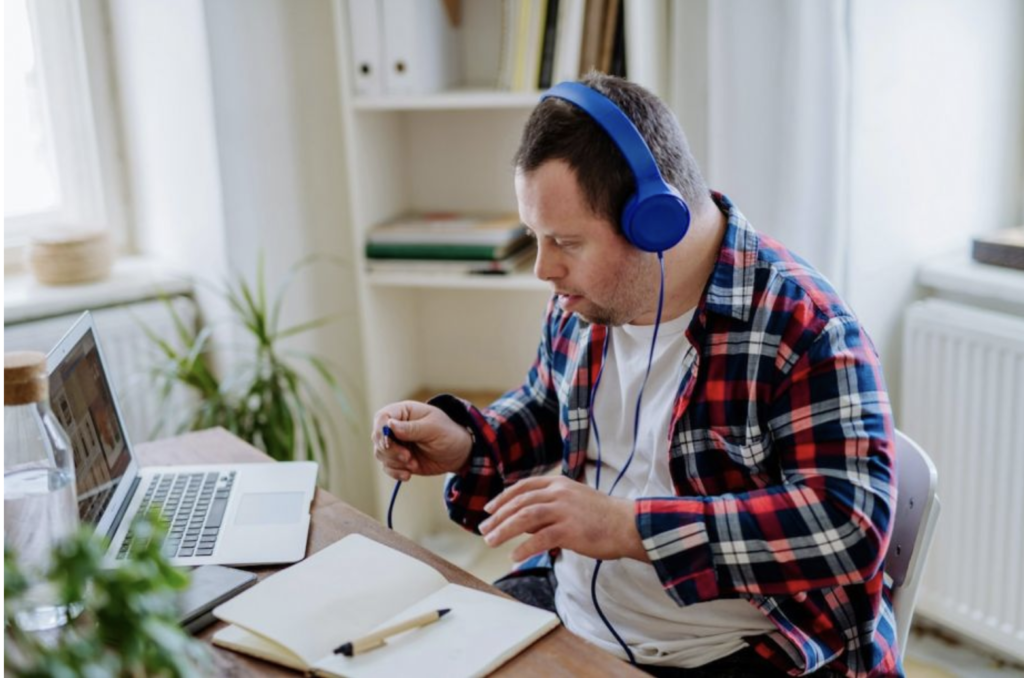 A man with IDD sits at a desk in front of his laptop with headphones on, preparing to work. 