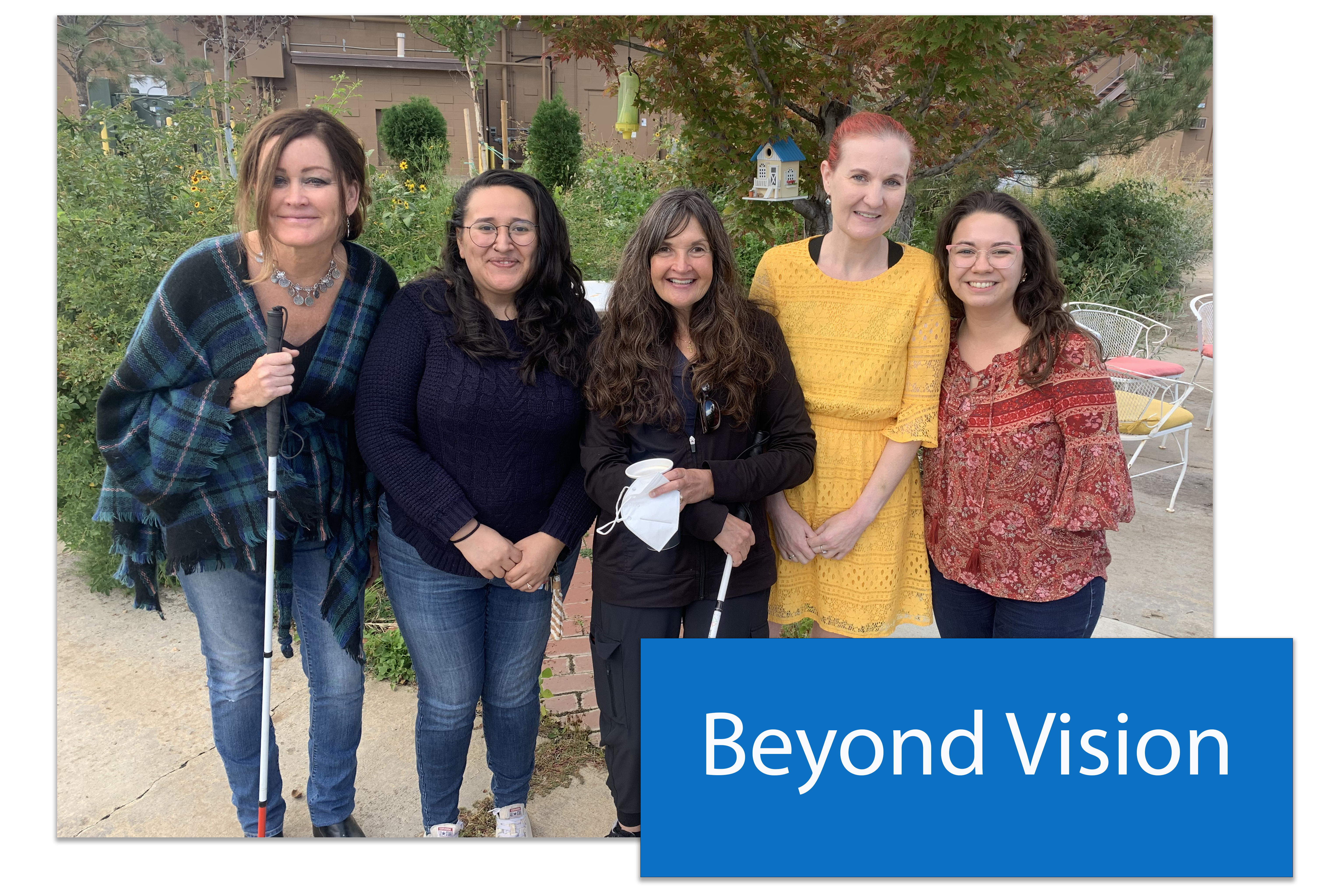 A button that says Beyond Vision placed in the lower right hand corner of an image of a group of five woman. They are the staff of the Beyond Vision program. Two of the women carry walking canes for the visually impaired.