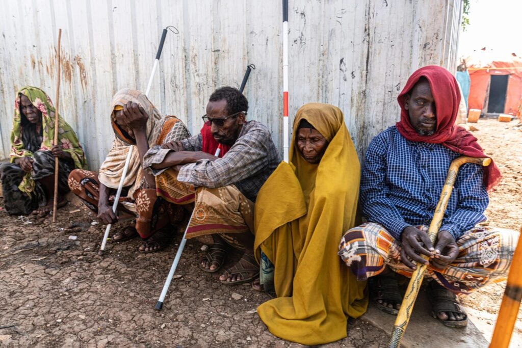 Displaced people who are blind crouching near a wall