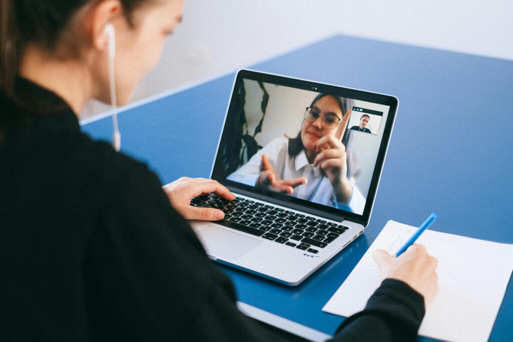 Two women speak to each other through a telehealth session on a laptop. The woman on the screen is using sign language.